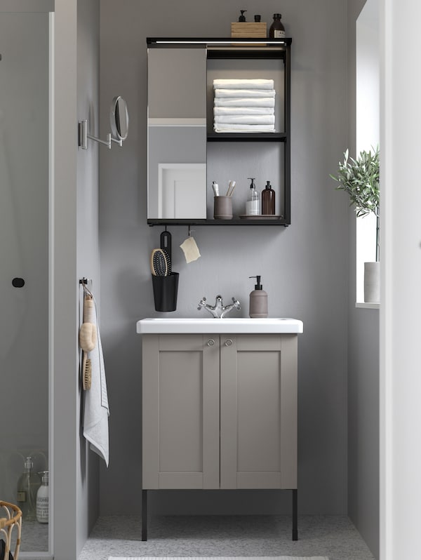 A bathroom with an ENHET 24" bathroom cabinet in anthracite grey, various bathroom articles hanging on the wall and a mirror.