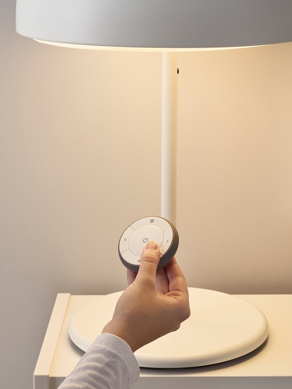 Person adjusting smart lighting with wireless remote for table lamp. 