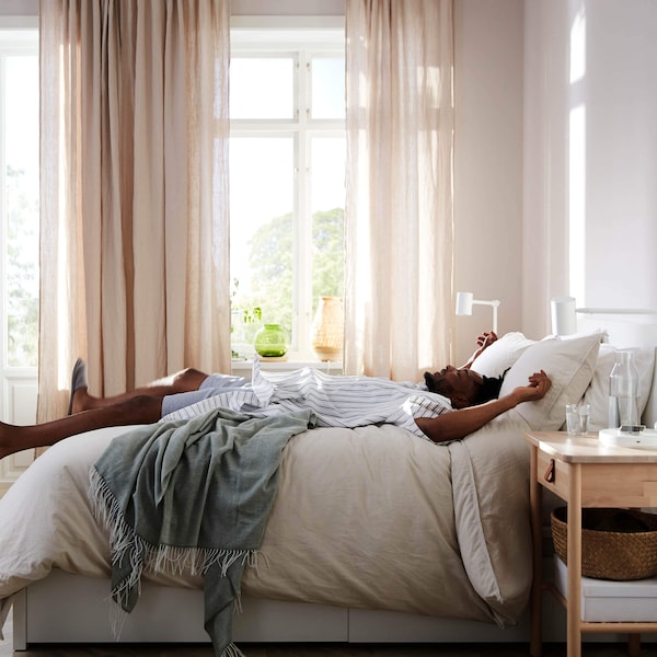 Person relaxing on a bed in a sunny, organized bedroom