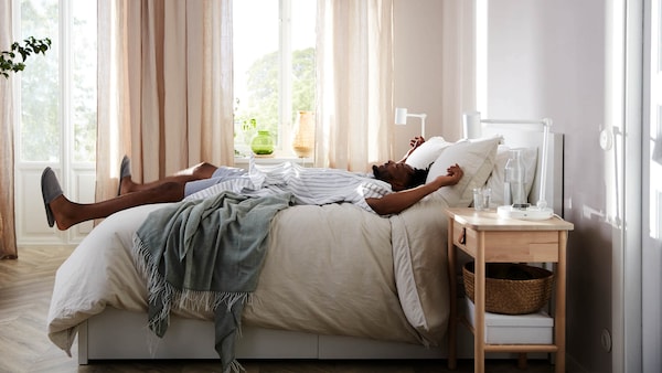 Person relaxing on a bed in a sunny, organized bedroom