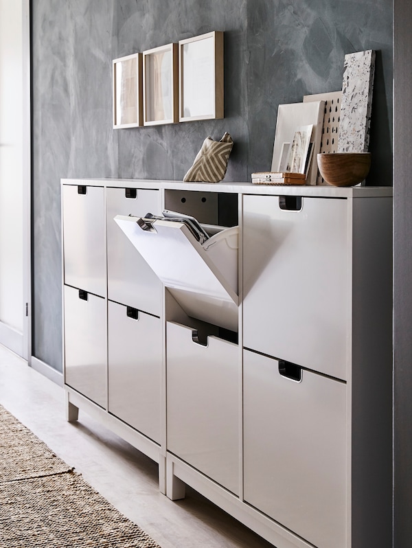 A hallway with two STÄLL shoe cabinets. Different objects sit on top and three framed pictures hang above.