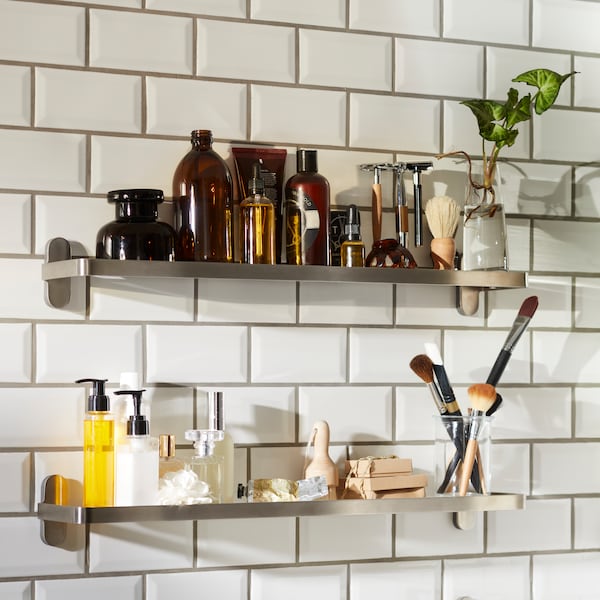 Beauty products and accessories for him and her on glass shelves in a bathroom with white tiles.