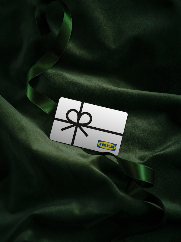 White IKEA gift card with a picture of a black ribbon on top of green velvet fabric.