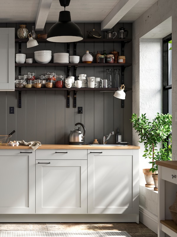 A farm style kitchen with KNOXHULT cabinets against a grey wood-panelled wall. Bowls, plates and jars are sitting on shelves.
