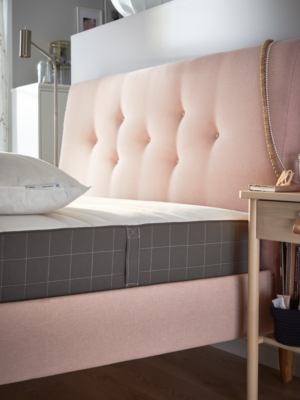 The head of a pale pink IDANÄS upholstered bed frame with a HÖVÅG pocket sprung mattress and a pillow on top.