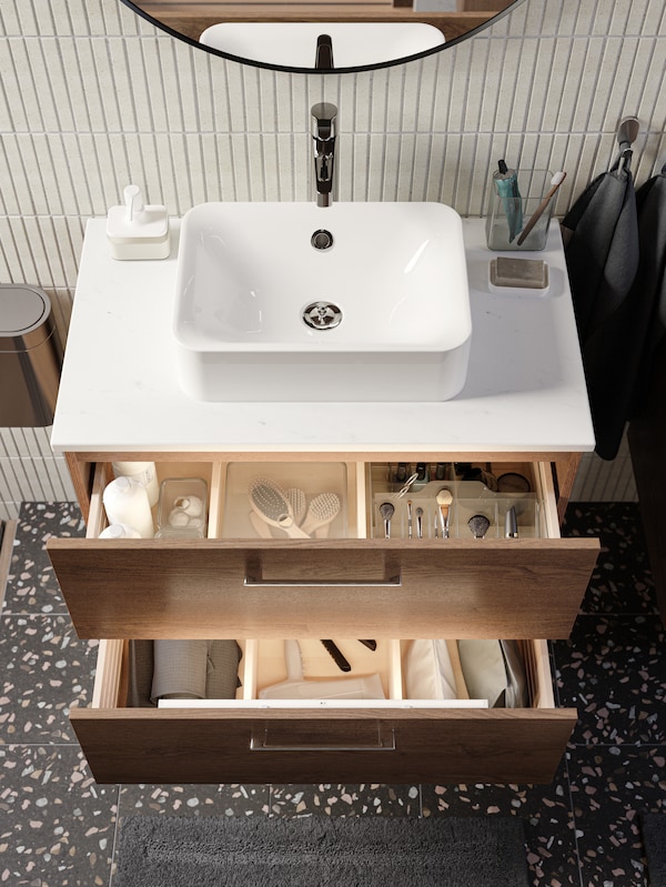 Sink drawers opened to reveal neatly arranged brushes in clear organizers, shampoo bottles, hairdryer and more.