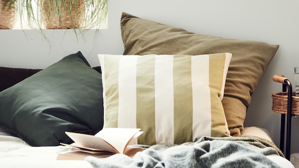 Cushions in different cushion covers including one in a striped HILDAMARIA cushion cover sit on a bed against a wall.
