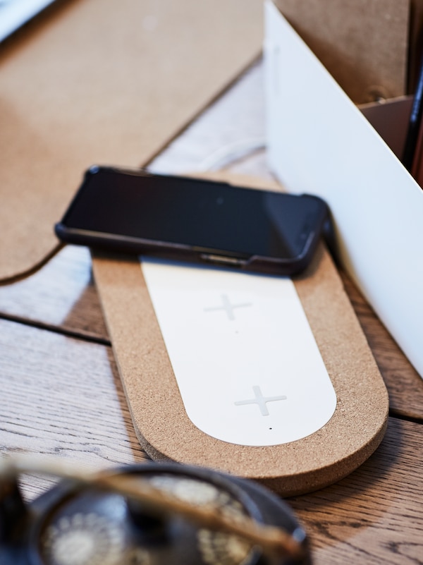 A mobile phone lies on top of a NORDMÄRKE triple pad for wireless charging on top of a desk.