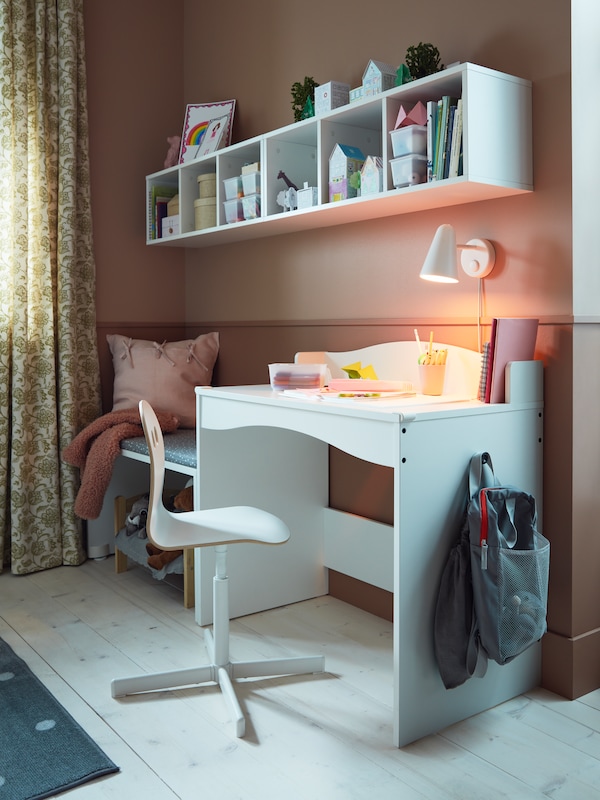 A VALFRED/SIBBEN children’s desk chair stands at a white SMÅGÖRA desk which is against a wall with two SMÅGÖRA shelf units.