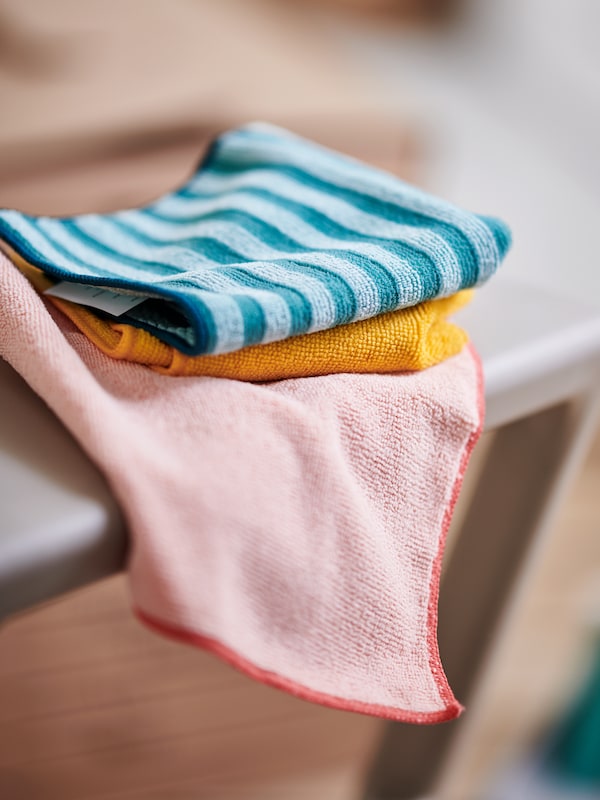 Three PEPPRIG microfiber cloths in different colors lie on top of each other on the edge of a table.