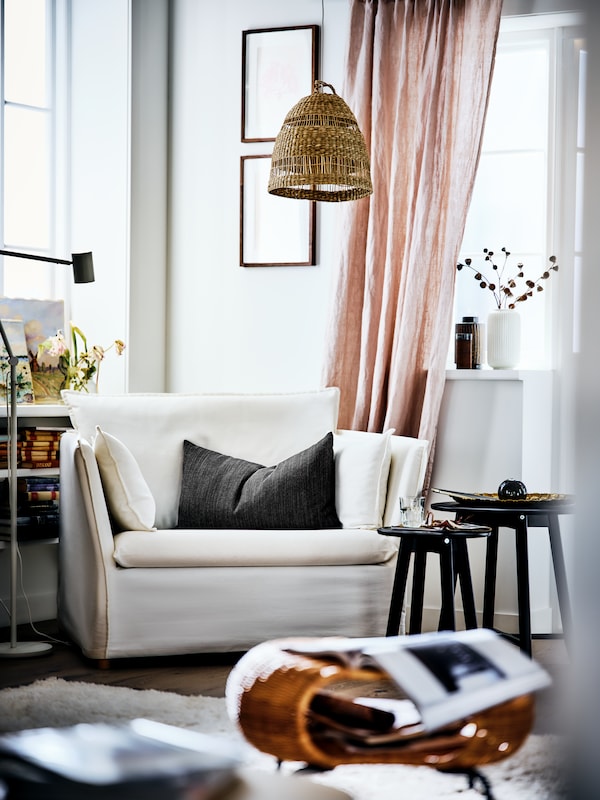 A BACKSÄLEN armchair in the corner of a bright living room with a pendant lamp overhead and a coffee table nest beside it.