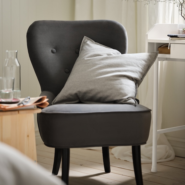 Part of a bedroom with a dark-grey REMSTA armchair, contrasting against an otherwise light color scheme.
