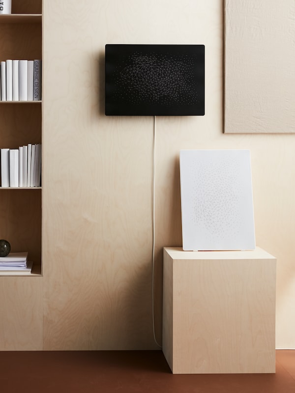 A black SYMFONISK picture frame with WiFi speaker attached to a wall above a white SYMFONISK picture frame with WiFi speaker.