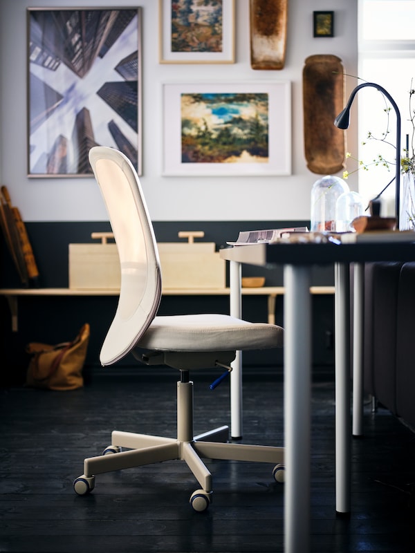 A beige FLINTAN office chair standing by a desk with a dark-grey LAGKAPTEN tabletop in a room with framed art on the walls.