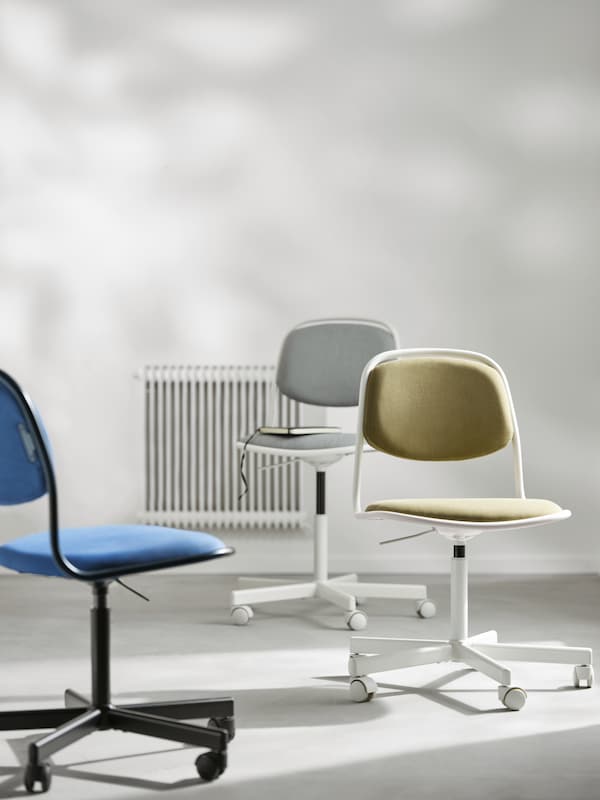 Three ÖRFJÄLL swivel chairs, one white and light grey, one white and yellow-green and one black and blue, placed in a room.
