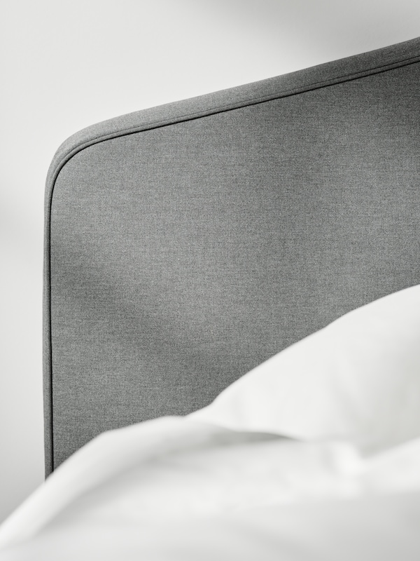 The headboard of a gray HAUGA upholstered bed, with a duvet and pillow in white ÄNGSLILJA bed linen next to it.