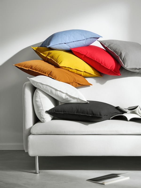 One end of a white sofa that has lots of cushions scattered on top of it, covered with different colour GURLI covers.