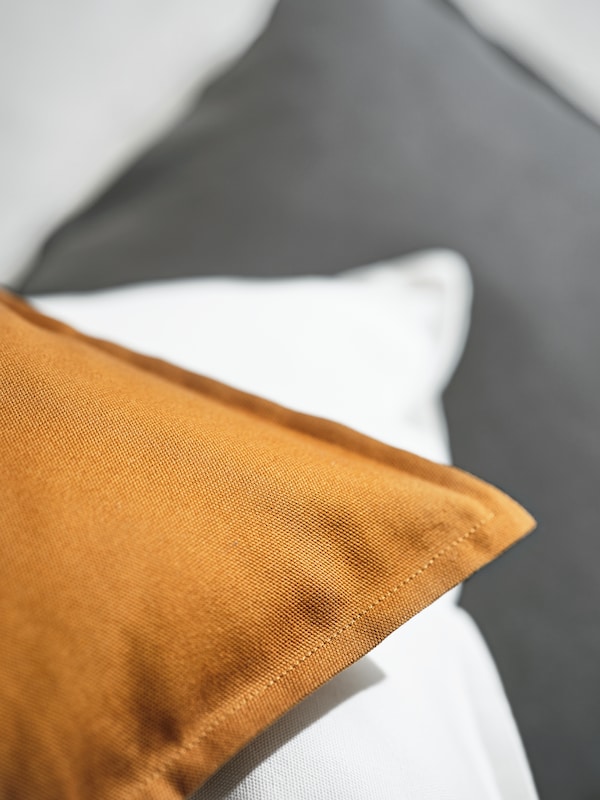 Three cushions layered across each other, covered with GURLI covers in brown-yellow, white and grey.