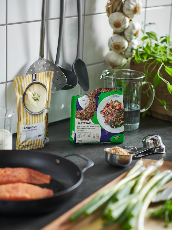 Packs of BÄSTISAR mix of grains with mushrooms and LÄCKERGOM lemon and dill sauce surrounded by cooking accessories.
