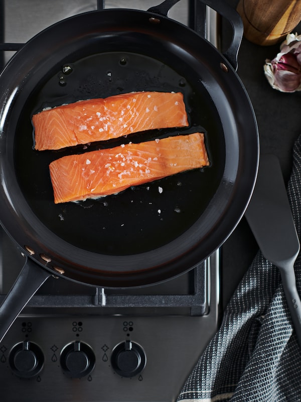 Two SJÖRAPPORT salmon fillets in a VARDAGEN carbon-steel frying pan placed on a gas hob.