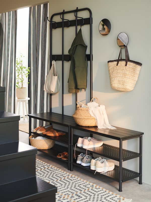 A PINNIG coat rack and shoe bench against a wall holding a coat, baskets and shoes. Two round mirrors are on the wall.