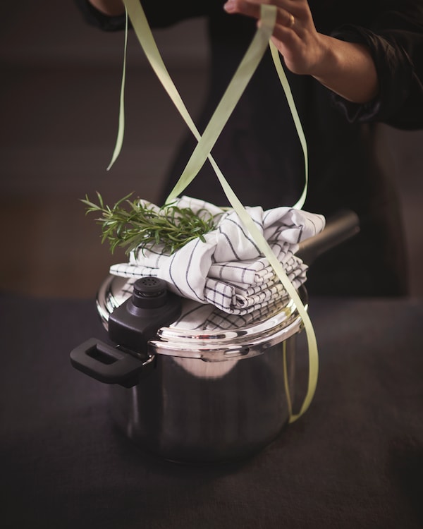 Person tying a green ribbon round a gift kit with tea towels and a pot.