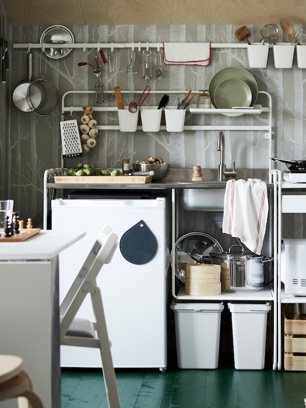 Kitchen utensils hang from hooks on a SUNNERSTA mini-kitchen. Brussel sprouts are being prepared on a butcher’s block.