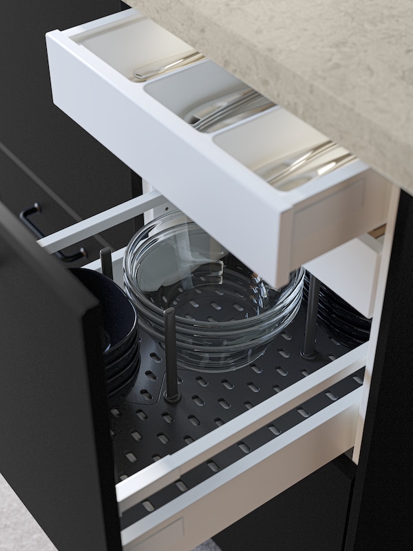 An open black kitchen drawer revealing bowls stacked in an UPPDATERA pegboard drawer organizer in anthracite.
