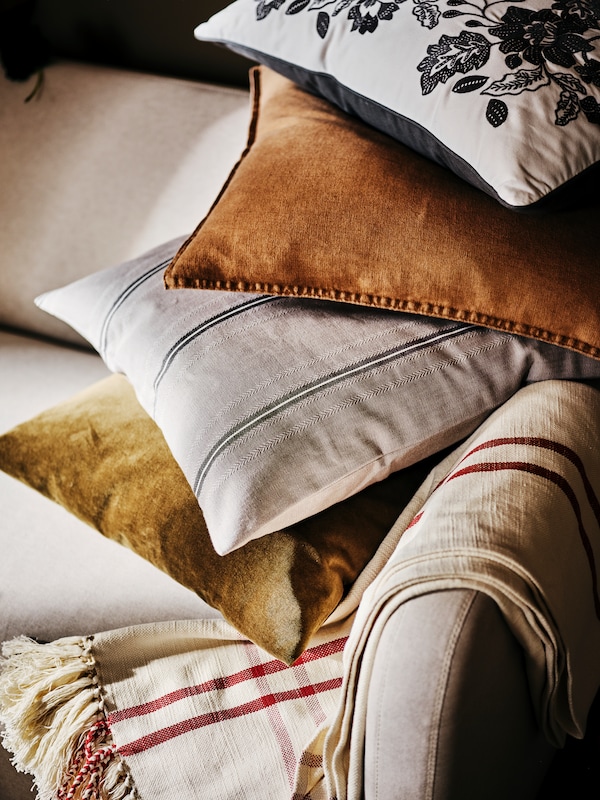 Four cushions, including one in a grey/white STORTIMJAN cushion cover, are piled on a LINANÄS sofa near a throw.