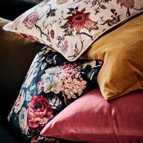 A cushion in a NÄSSELKLOCKA cushion cover sits on top of cushions in LEIKNY and SANELA cushion covers.