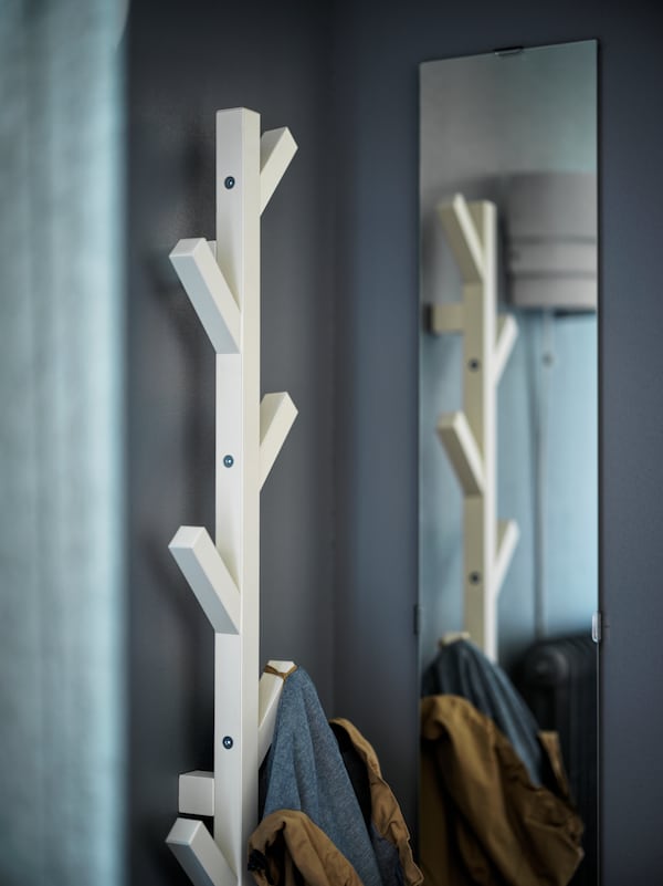 A white TJUSIG hanger with a jacket hanging from it is attached to a wall near a FREBRO mirror which reflects its image.
