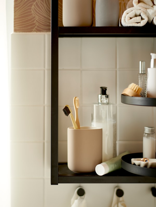 A bathroom with an ENHET wall shelf with EKOLN toothbrush holder in beige, toiletries and towels stored on the shelves.