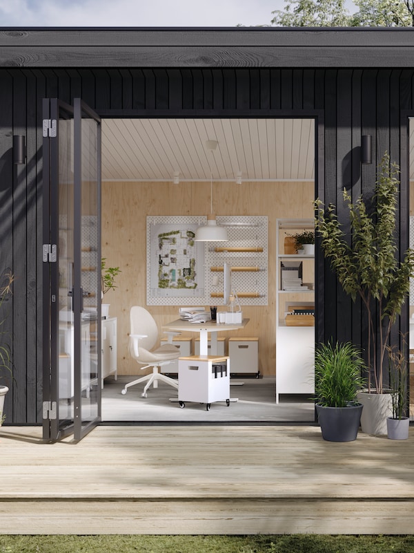 A garden studio with open doors showing a desk and chair work area, TROTTEN storage units on castors and cabinets.