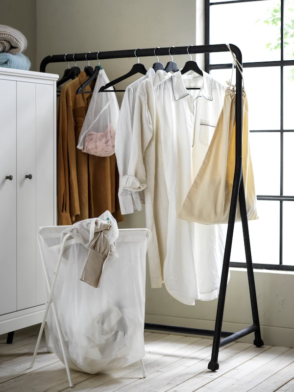 In a corner of a softly lit wood-floor room stands a black TURBO clothes rack with garments hung on black BUMERANG hangers.
