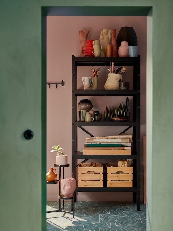 A black BROR storage unit stands on a tiled floor and displays ceramics, tableware, papers and wooden boxes.