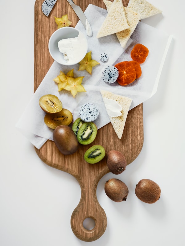 An ARTISTISK chopping board holding different exotic fruits like kiwis and star fruit placed together with slices of bread.