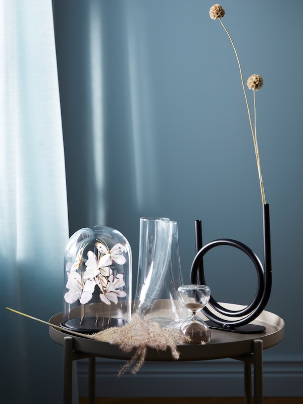 A display on a side table with small decorative objects like a glass dome with artificial butterflies and vases.