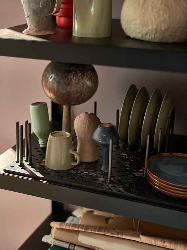 A pegboard is placed on a BROR shelving unit and used to store colorful cups, plates and other ceramic items.