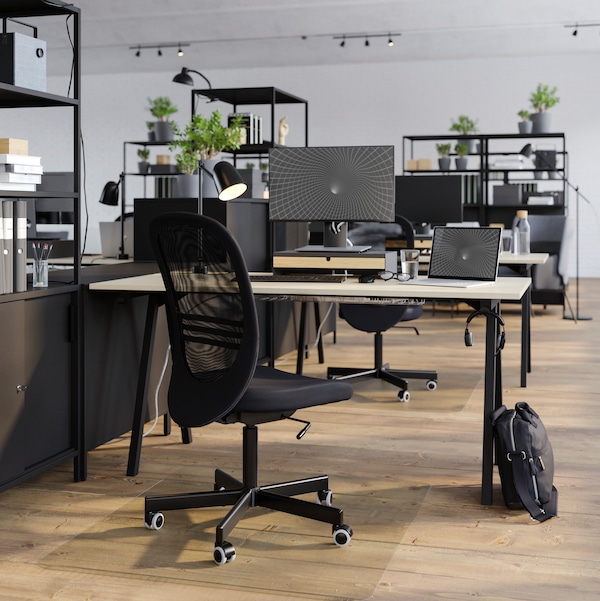 A TROTTEN desk and black FLINTAN office chair in a light open plan office that’s divided up with open shelving and cabinets.