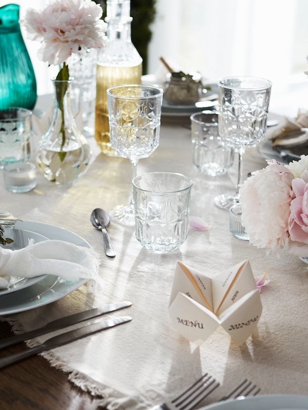 A festive table laid with SÄLLSKAPLIG wine glasses, water glasses and carafes among a variety of table decorations.
