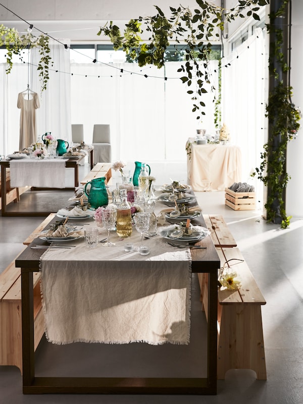 A festive table laid for a formal occasion with benches for guests to sit on placed in a light open space with other tables.