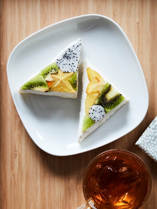 A white plate with triangle-shaped sandwiches made with fruits like kiwi and star fruit, all placed on a wooden surface.