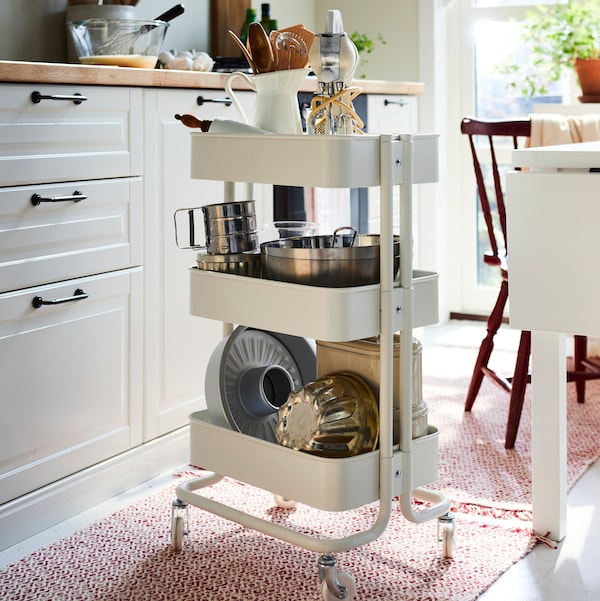 A white RÅSKOG kitchen cart has its shelves full of pots, pans, and an IDEALISK sifter.