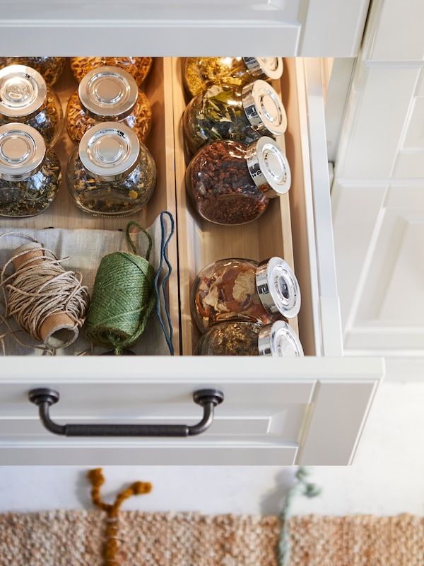 Glass jars of herbs and rolls of string sit in UPPDATERA bamboo utensil trays inside a kitchen drawer.