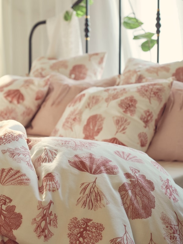 A SAGSTUA bed with VITPYROLA bed linen, which has a coral and seashell pattern, and two cushions with AINA cushion covers.