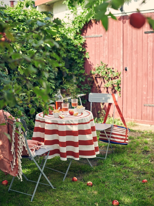 A small round table is set outside with a bright SOMMARFLÄDER tablecloth and delicious juice and breakfast foods.