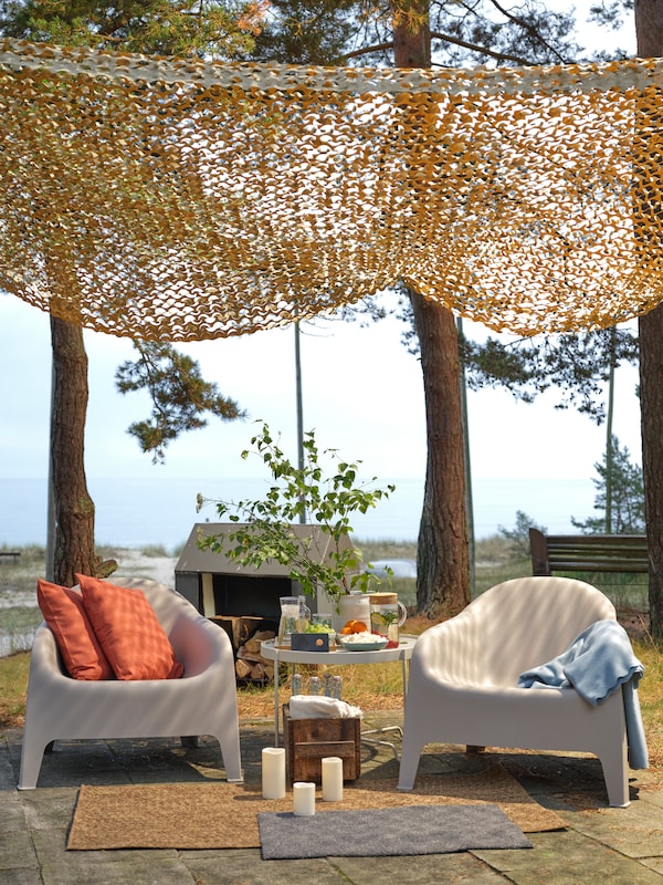 Two SKARPÖ outdoor armchairs are on a stone patio. A KROKHOLMEN outdoor coffee table is between the two chairs.