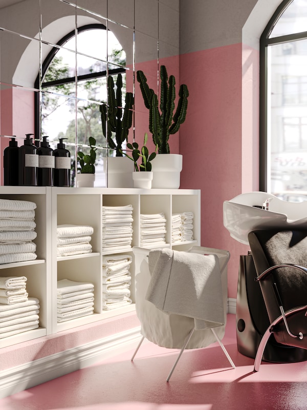 A hair salon with white KALLAX shelving units with folded white towels on the shelves, and potted cactus plants on top.