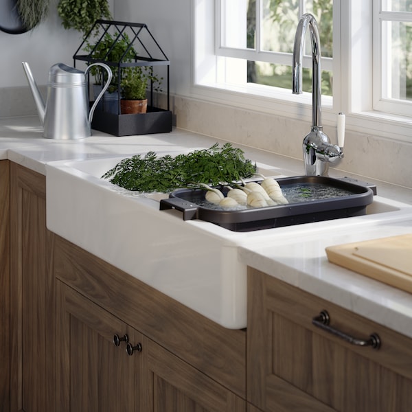A white HAVSEN sink in a traditional style kitchen with a washing up bowl inside filled with water and vegetables.