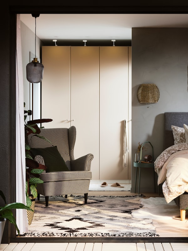 A sunny bedroom with a STRANDMON wing chair in front of a PAX/REINSVOLL wardrobe combination near an IDANÄS upholstered bed.